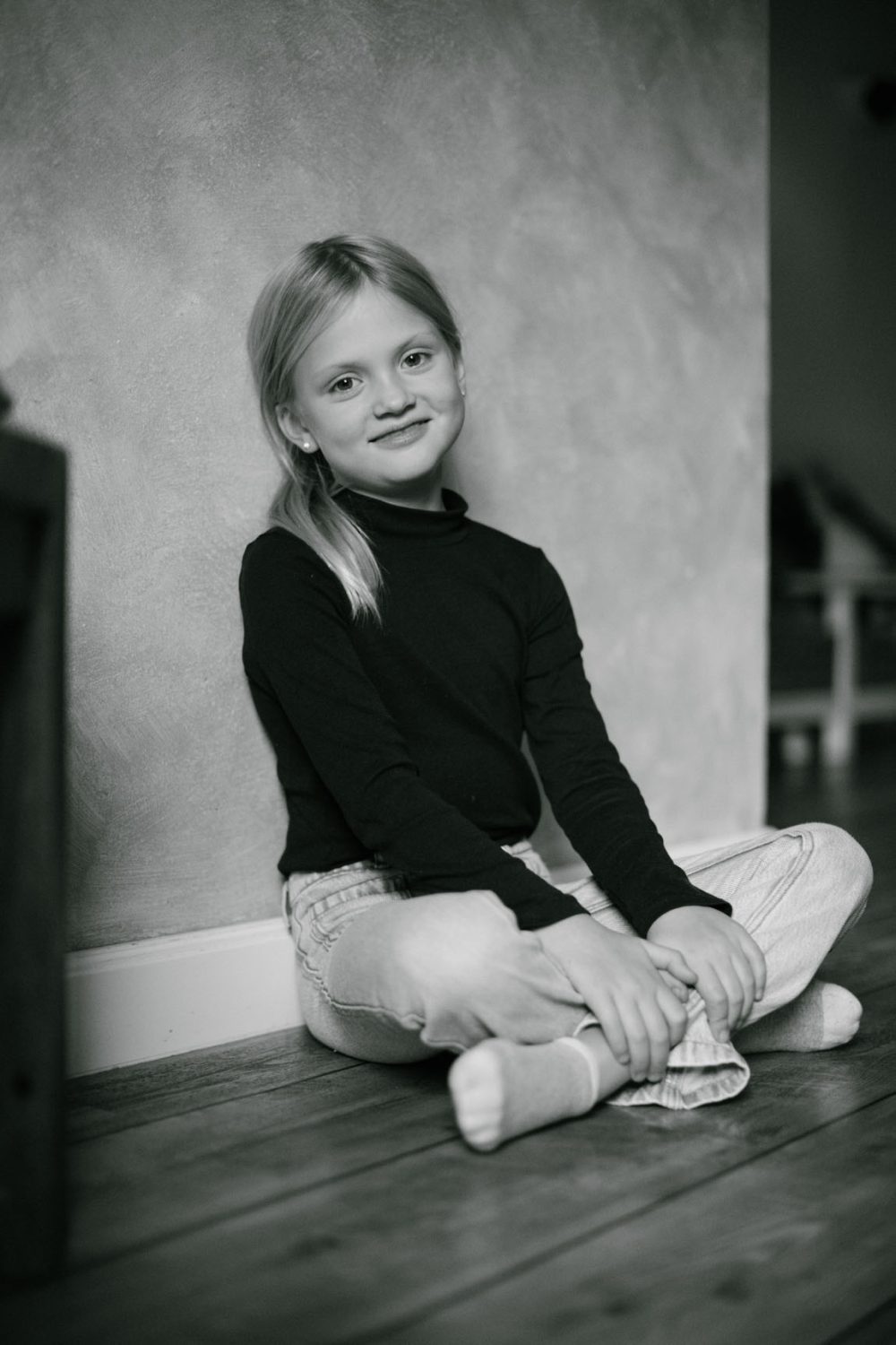 Blondes Mädchen sitzt vor einer Wand und lächelt